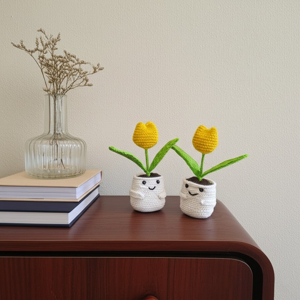 Two small crocheted plants with yellow flowers in white pots on a wooden surface.