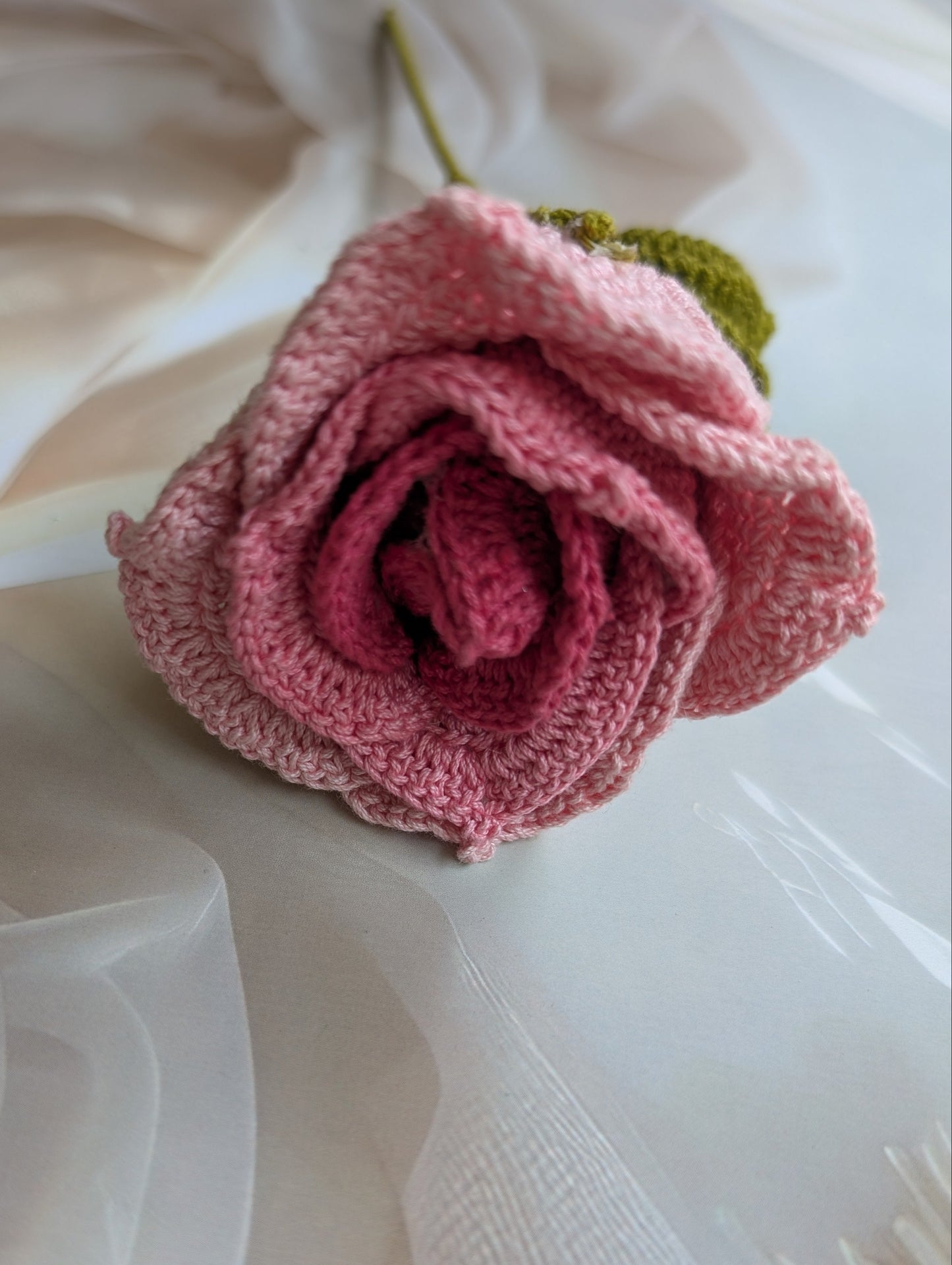 Knitted pink rose on a white fabric background