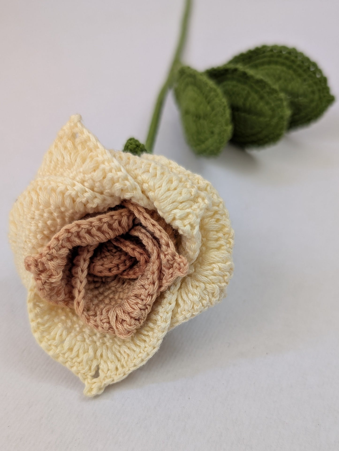 Crocheted rose with a gradient from beige to brown on a light background