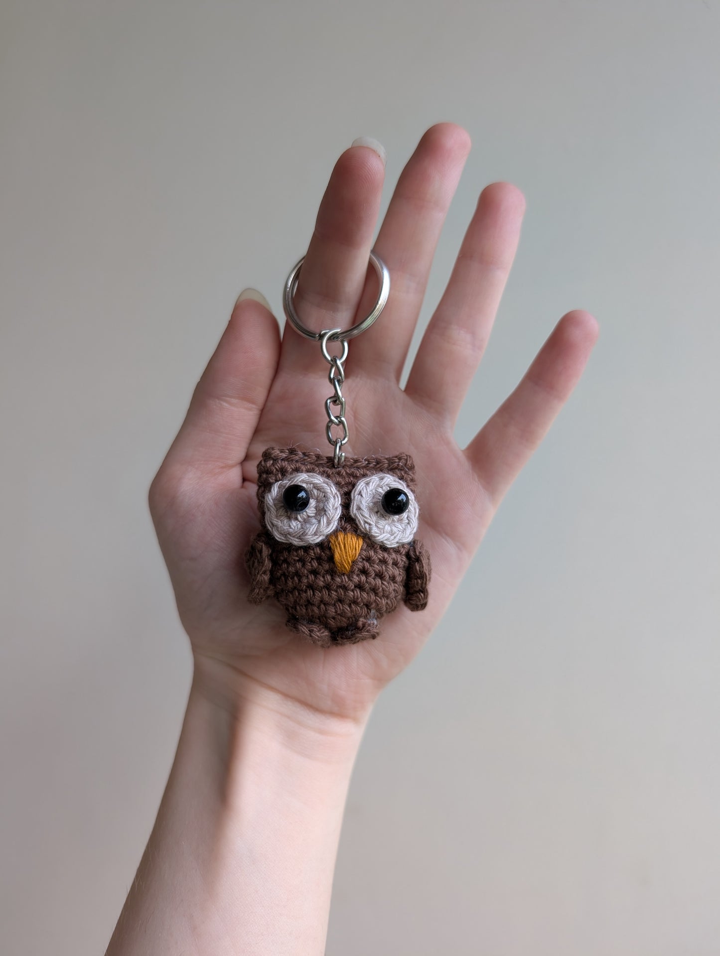 Hand holding a crochet owl keychain against a plain background