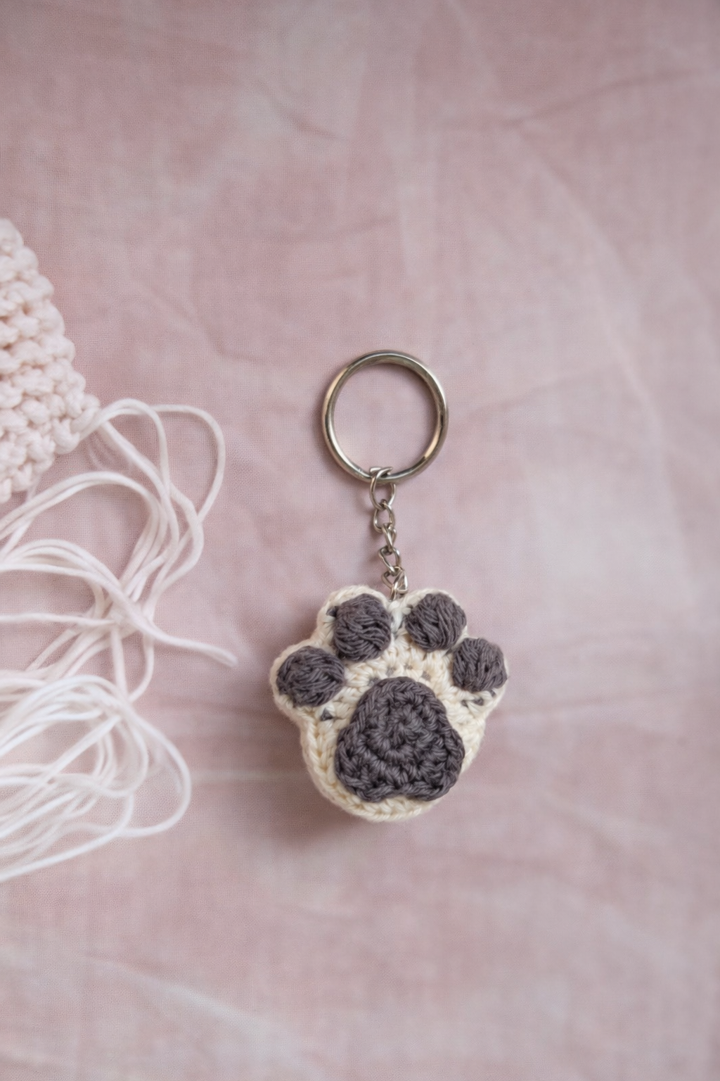 Crocheted paw print keychain on a pink surface