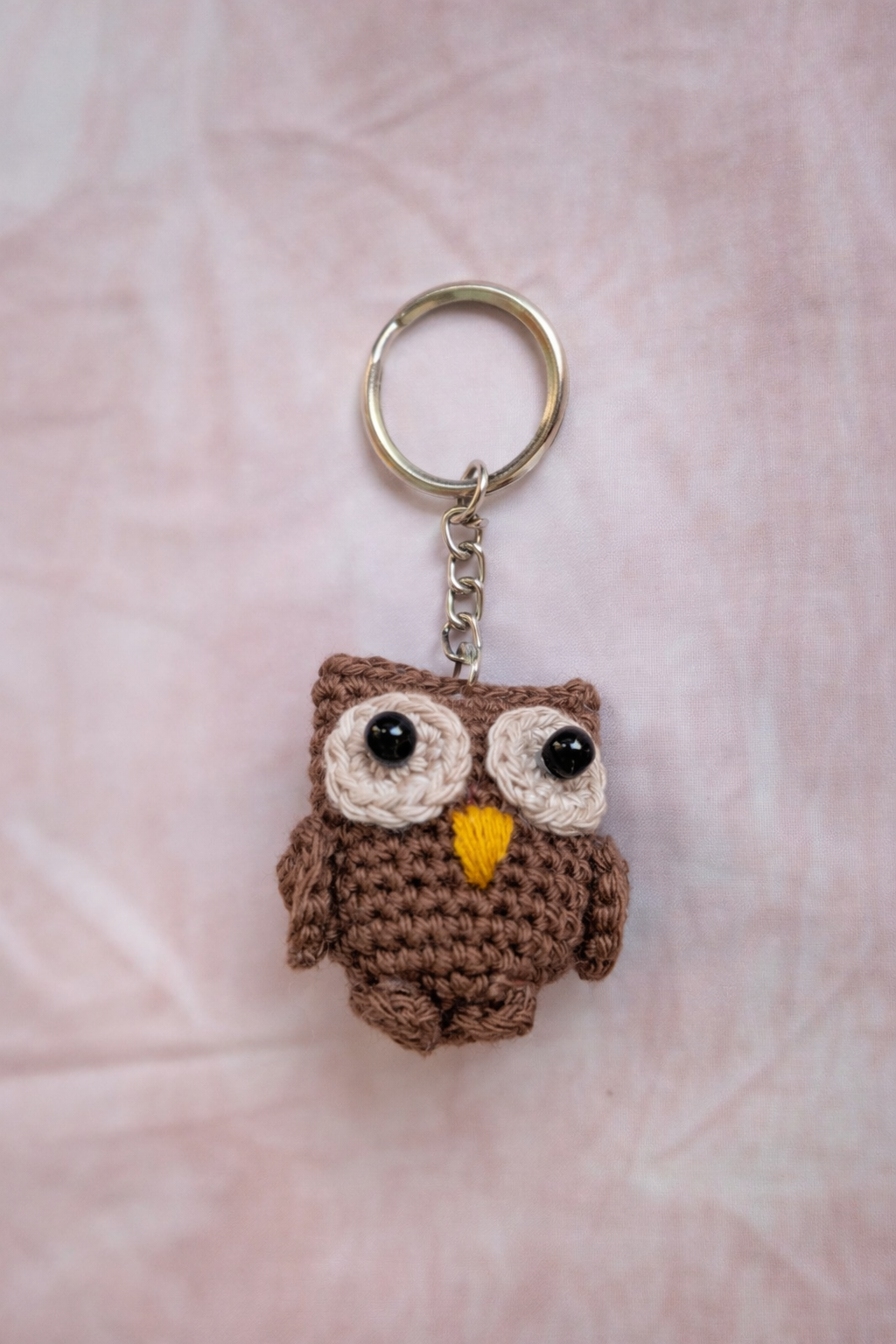 Crocheted owl keychain on a pink fabric background