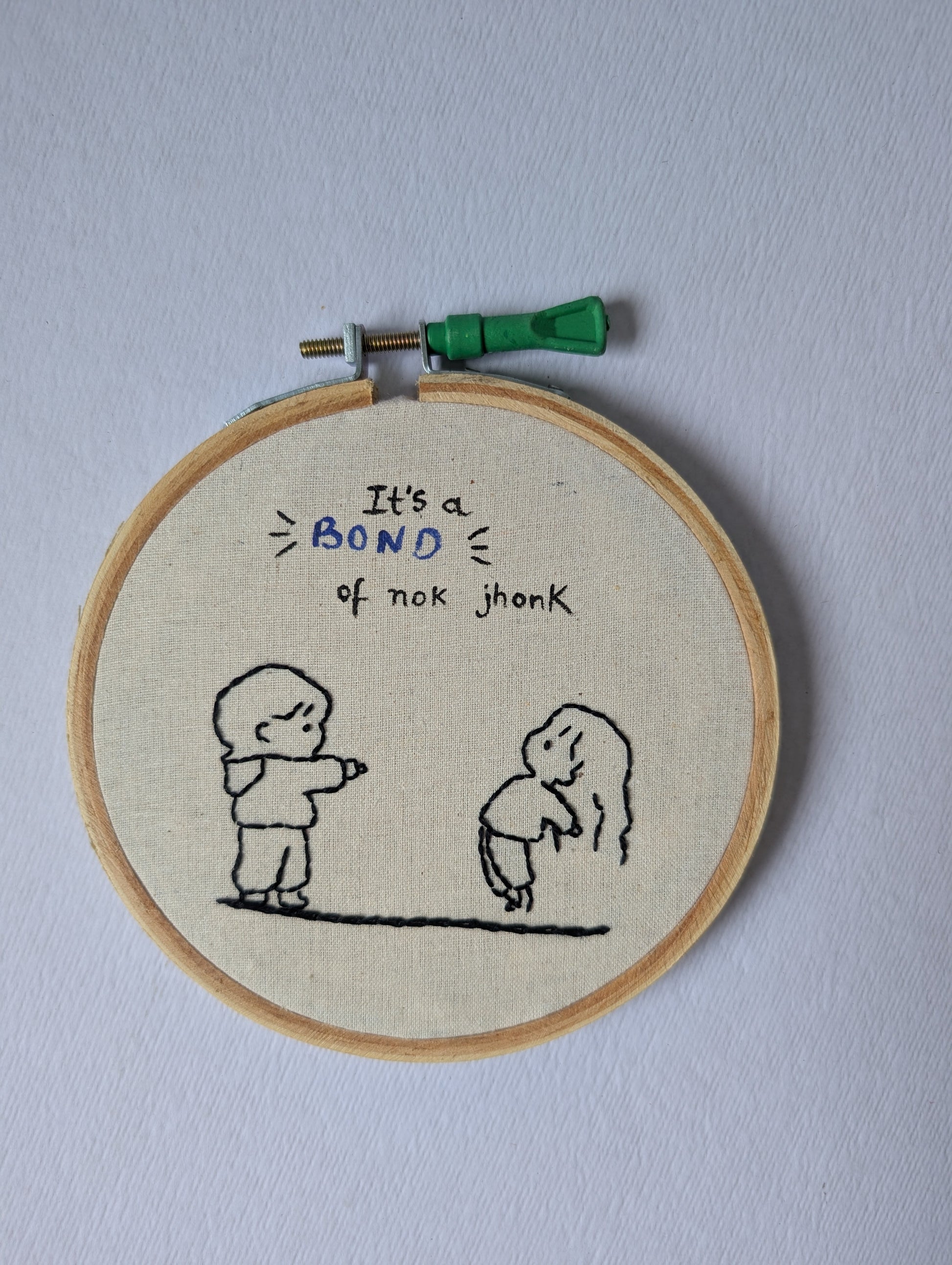 Embroidery hoop with embroidered text and illustrations on a plain background