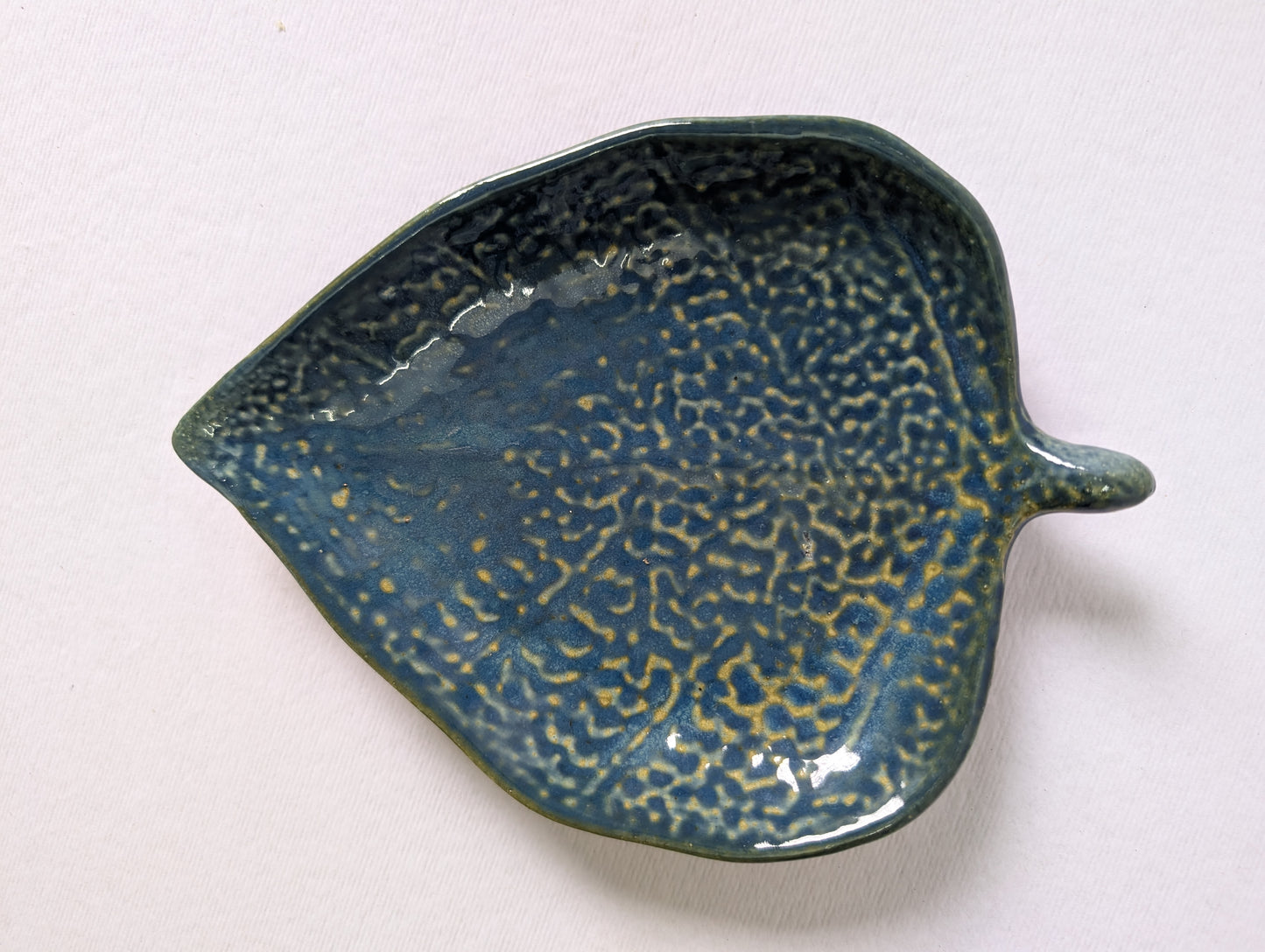 Ceramic leaf-shaped dish with textured blue glaze on a white background
