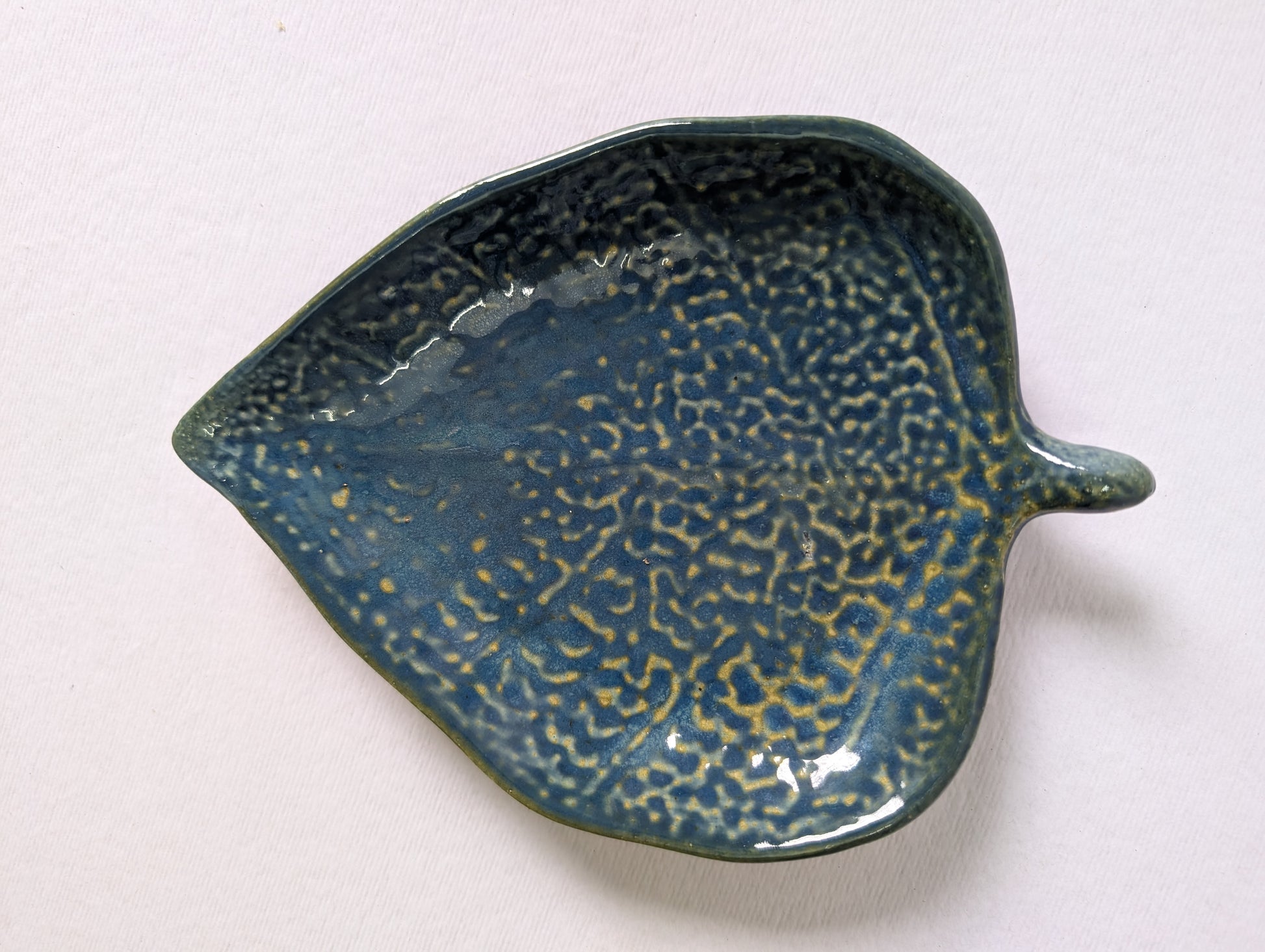 Ceramic leaf-shaped dish with textured blue glaze on a white background