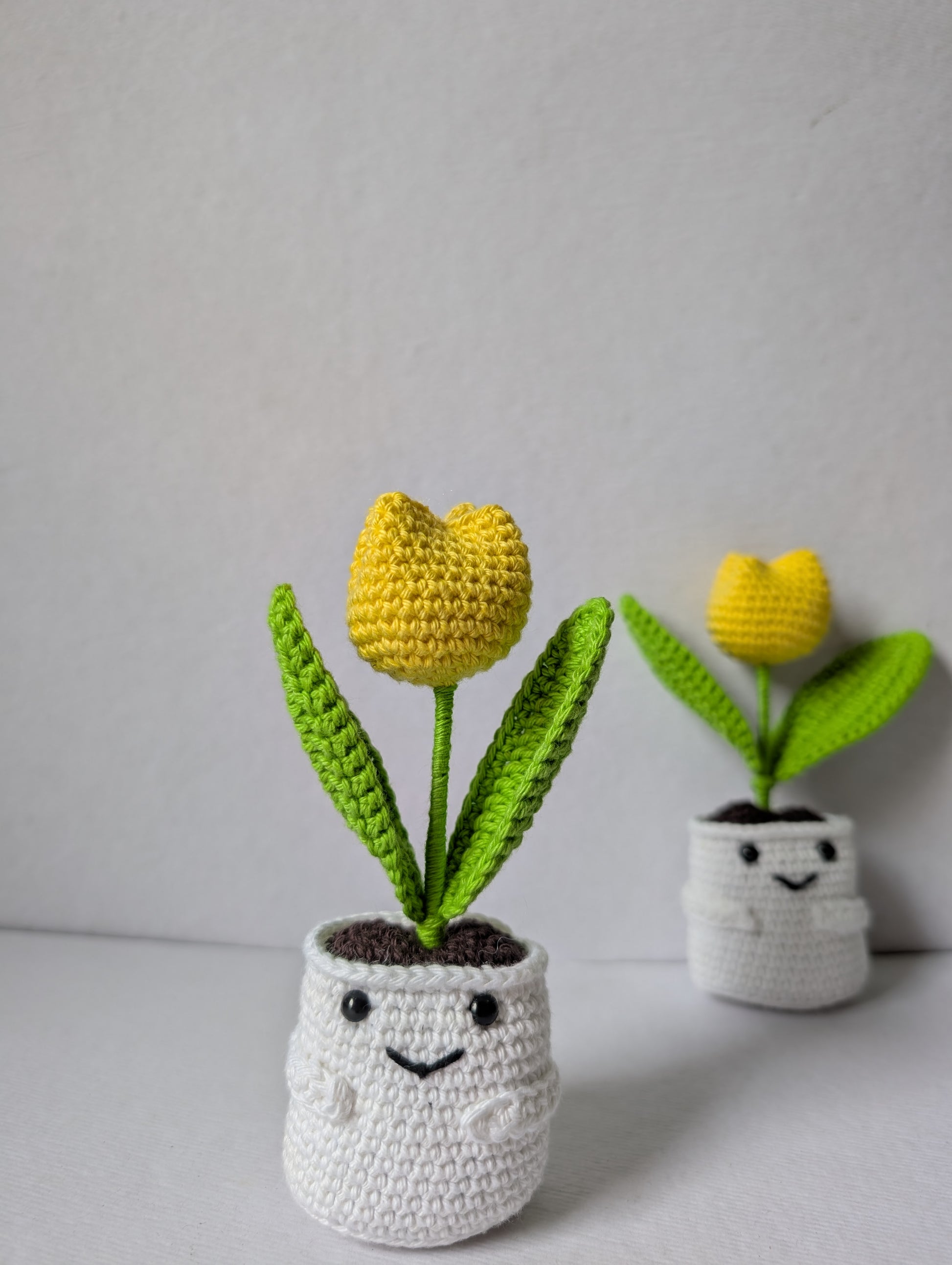 Two crocheted tulips in white pots on a light gray background