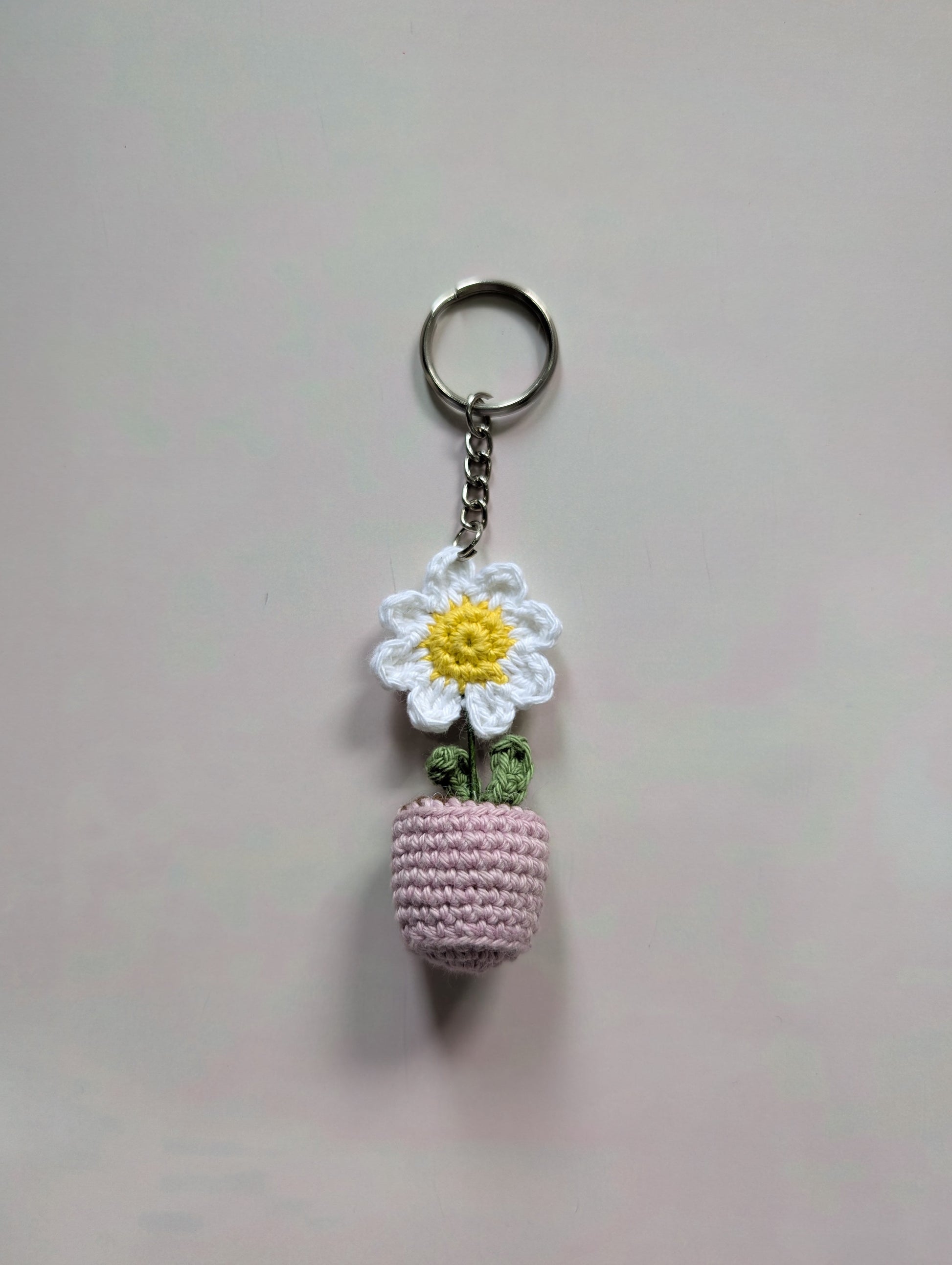 Keychain with a small pink crocheted ball and white flower charm on a light gray background
