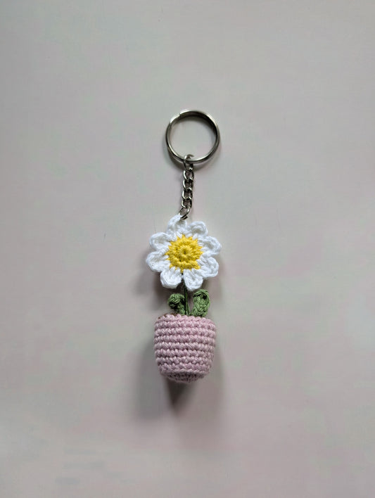 Keychain with a small pink crocheted ball and white flower charm on a light gray background